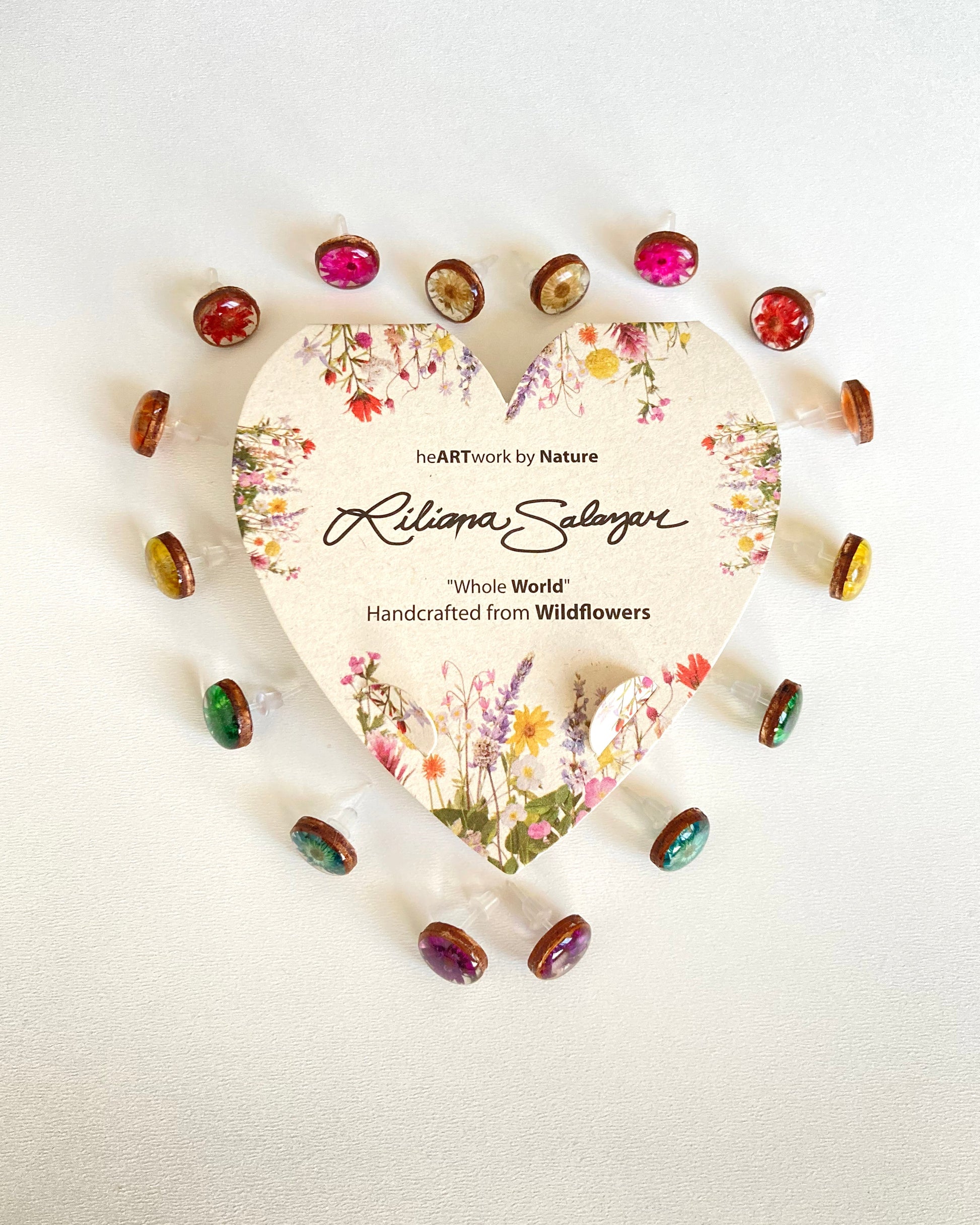 Heart-shaped packaging with floral design and small wildflower framed in wood earrings in rainbow color order on a white background